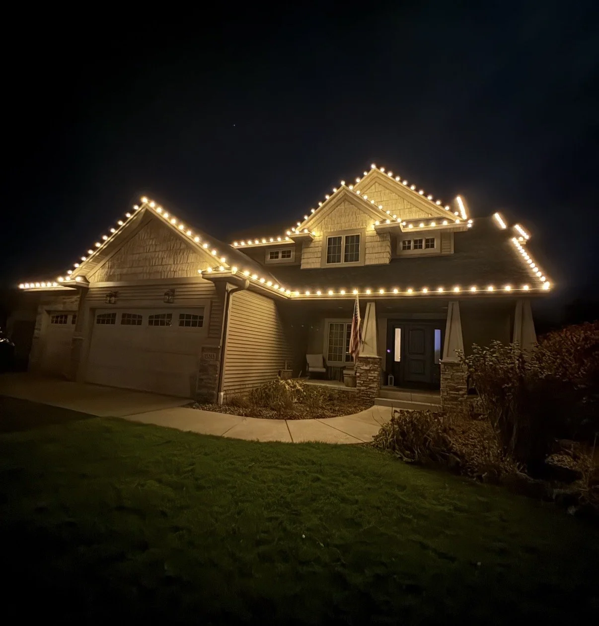 A two-story house illuminated with Christmas lights outlining the roof and windows at night.