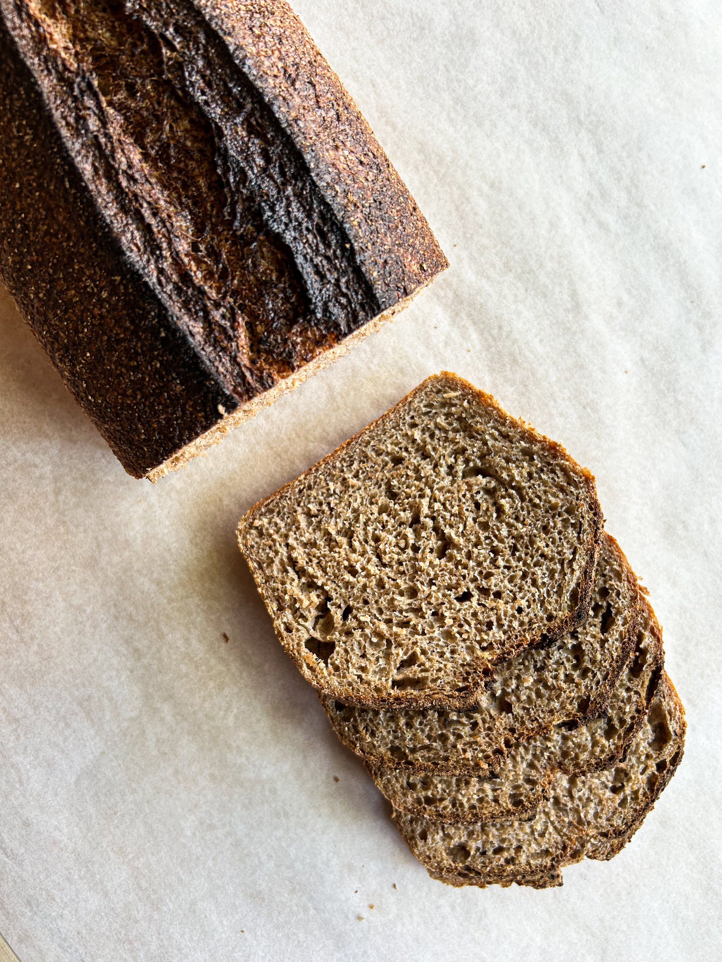 Sliced loaf of banana bread on white surface with a darker, uncut loaf in the background.