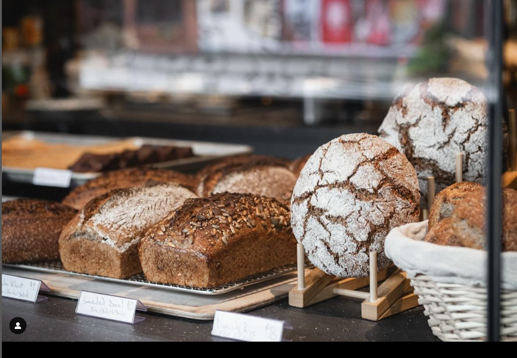 Display of various baked bread and pastry loaves in a bakery shop, including crusty bread, bread with seeds, and cracked sugar-dusted bread, in a bakery display case.