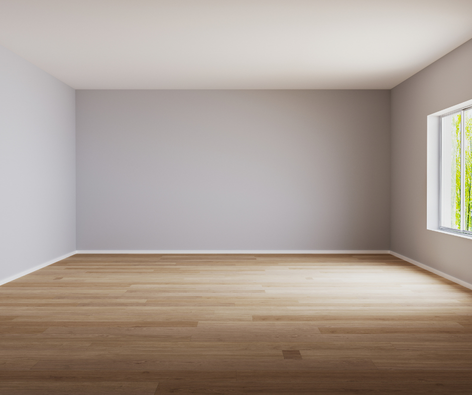 A clean, empty room with light gray walls, hardwood flooring, large window with sunlight, and a view of green trees outside.