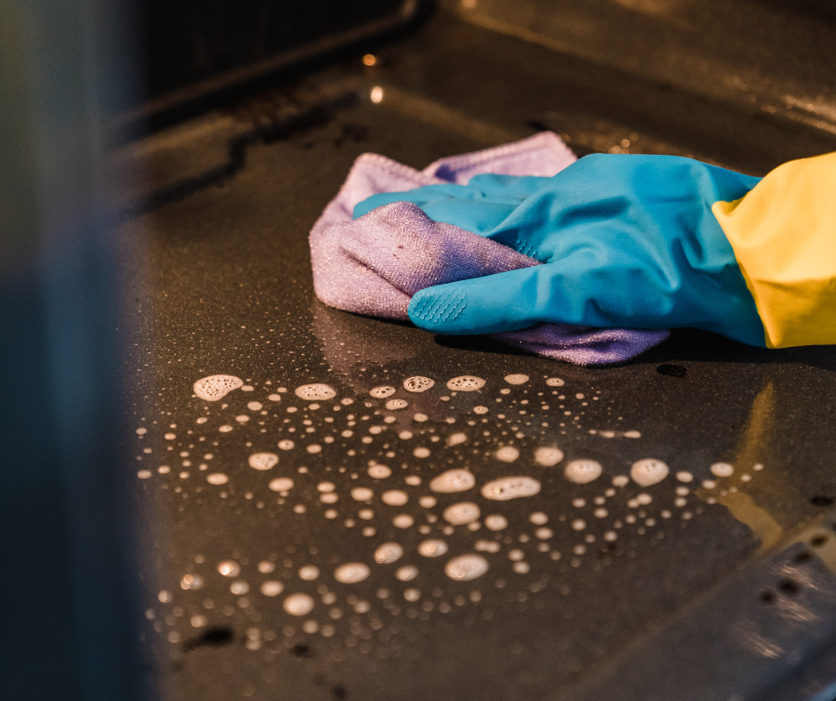 A person wearing a blue glove and yellow sleeve cleaning a black surface with a purple cloth, with soap suds and bubbles visible.