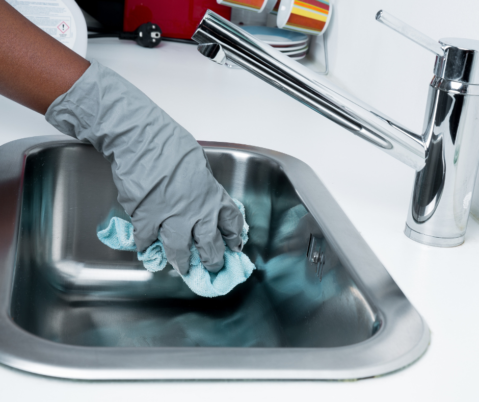 Person wearing a gray glove cleaning a stainless steel kitchen sink with a blue cloth.