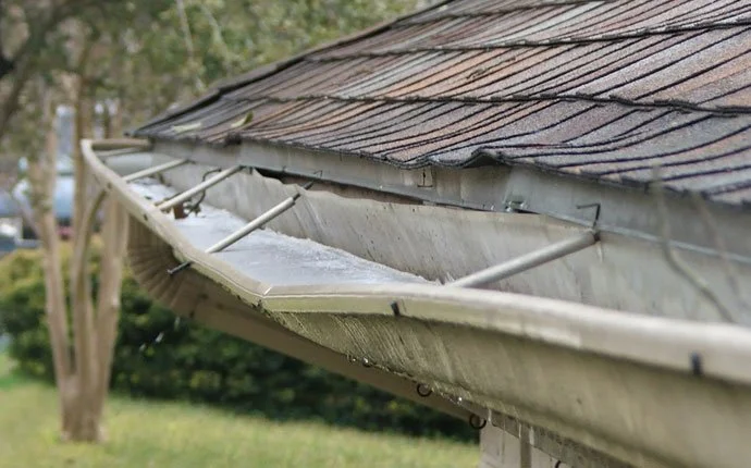 Close-up of a house's gutter system with water droplets and rain on the roof shingles.