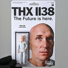 Toy figure of a bald man in a white suit next to a large portrait of the same man with one eye.