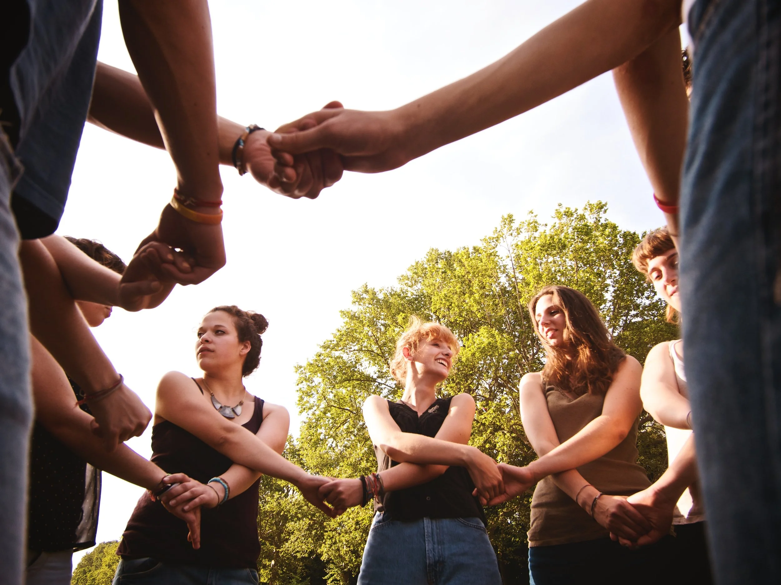 Group of young women standing in a circle outdoors, holding hands and smiling.