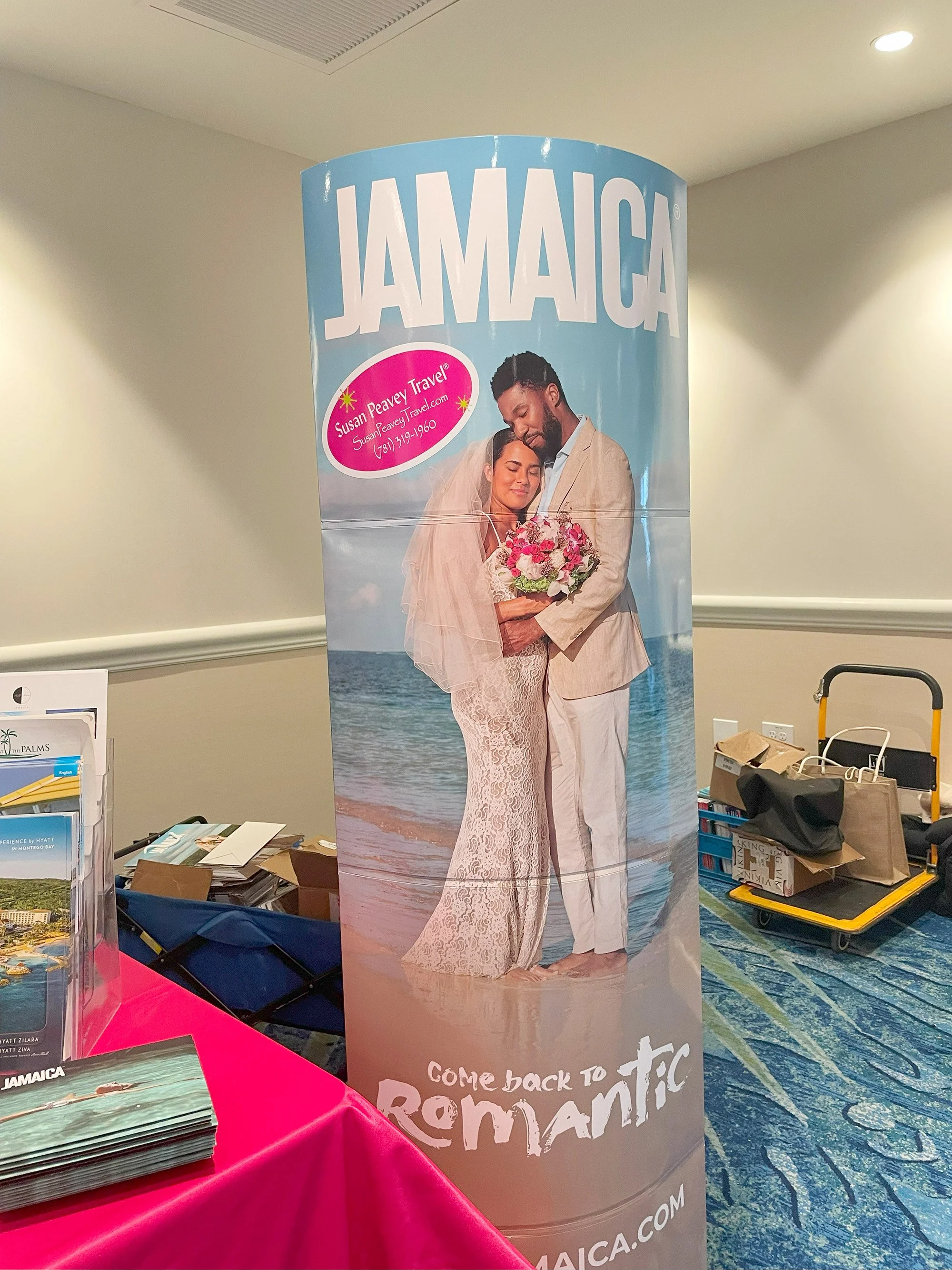 A large promotional banner displaying a couple in wedding attire embracing on a beach with ocean in the background. The banner promotes Jamaica and a travel company, Susan Peavey Travel, with a tagline encouraging return to romantic Jamaica.