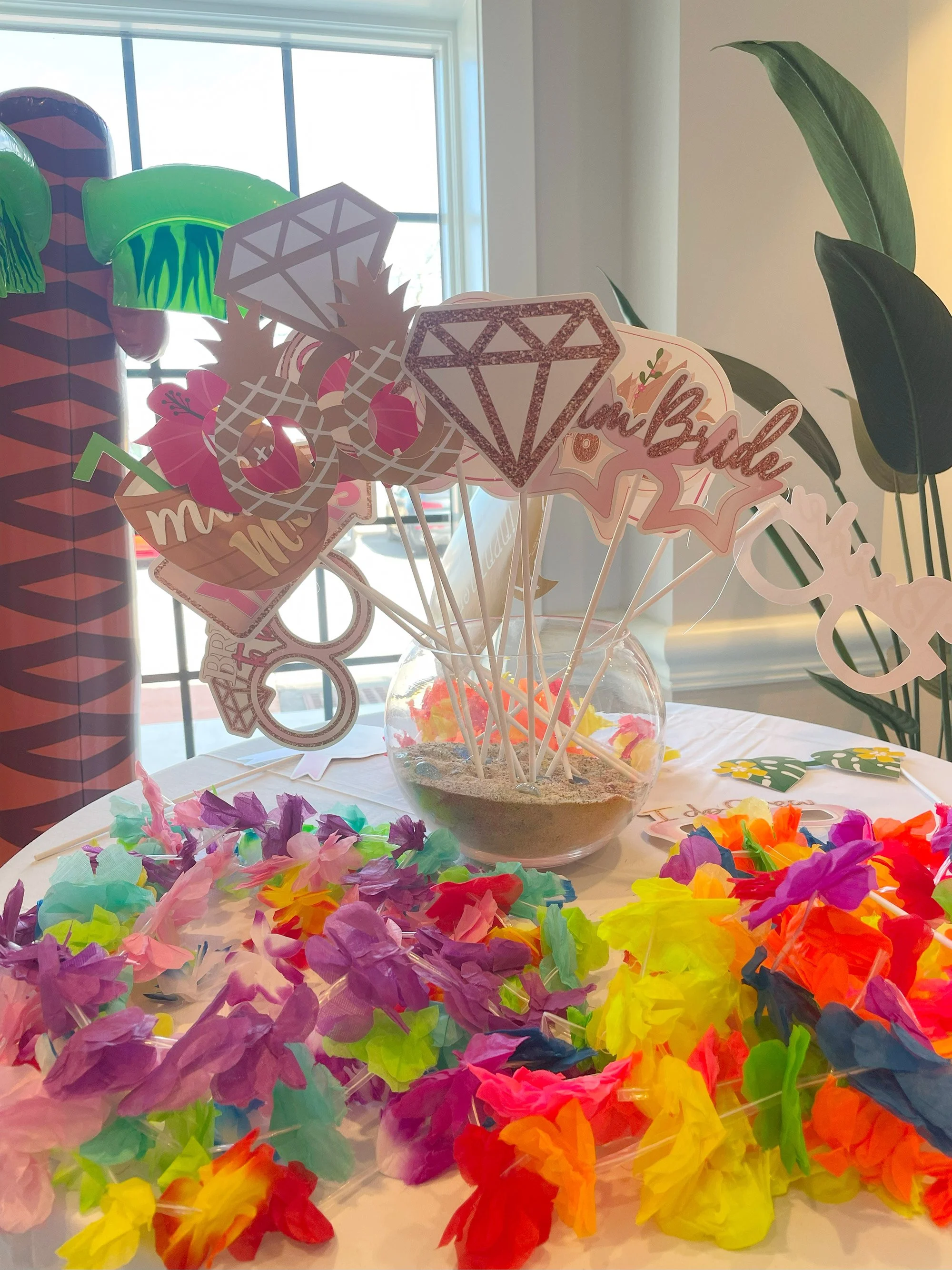 Colorful tissue paper flowers and rainbow-themed decorations on a table, with a window in the background.