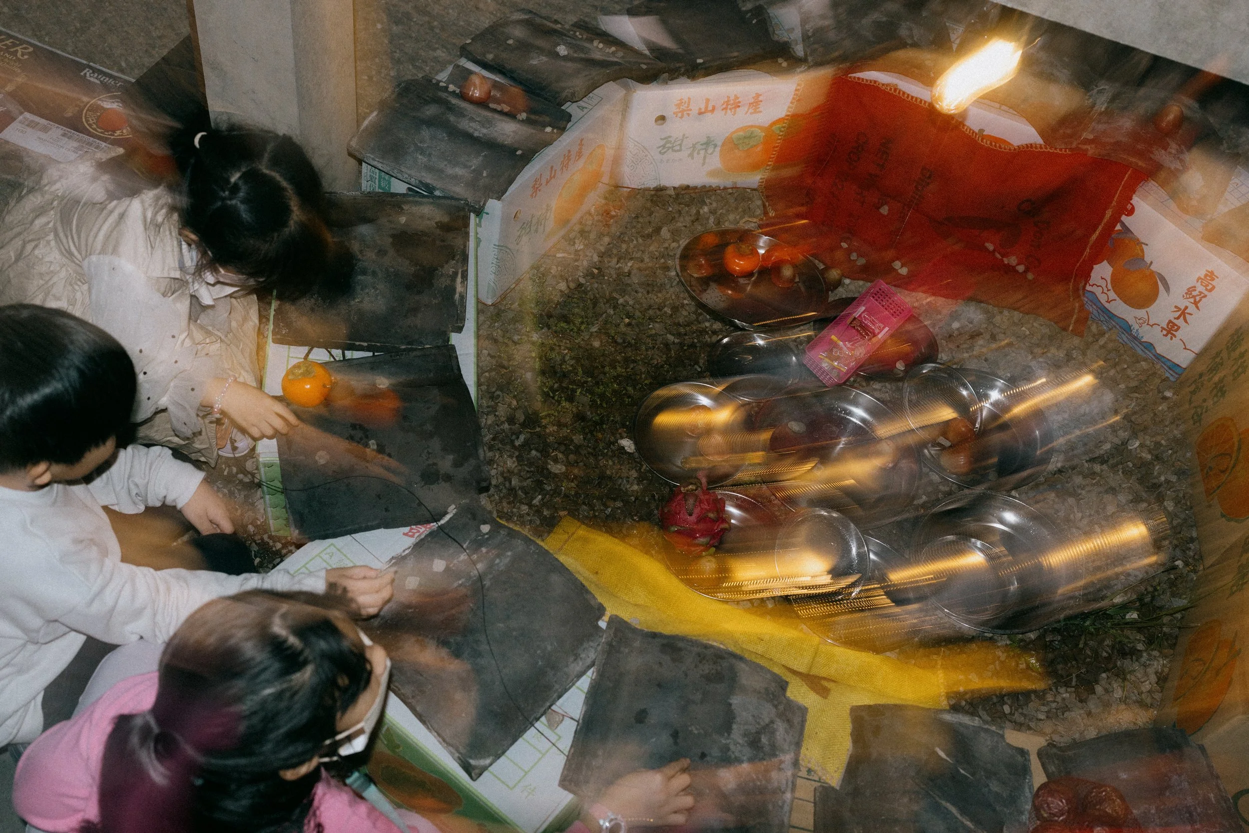 Children or people looking at a small outdoor shrine or offering display with fruit and small objects.