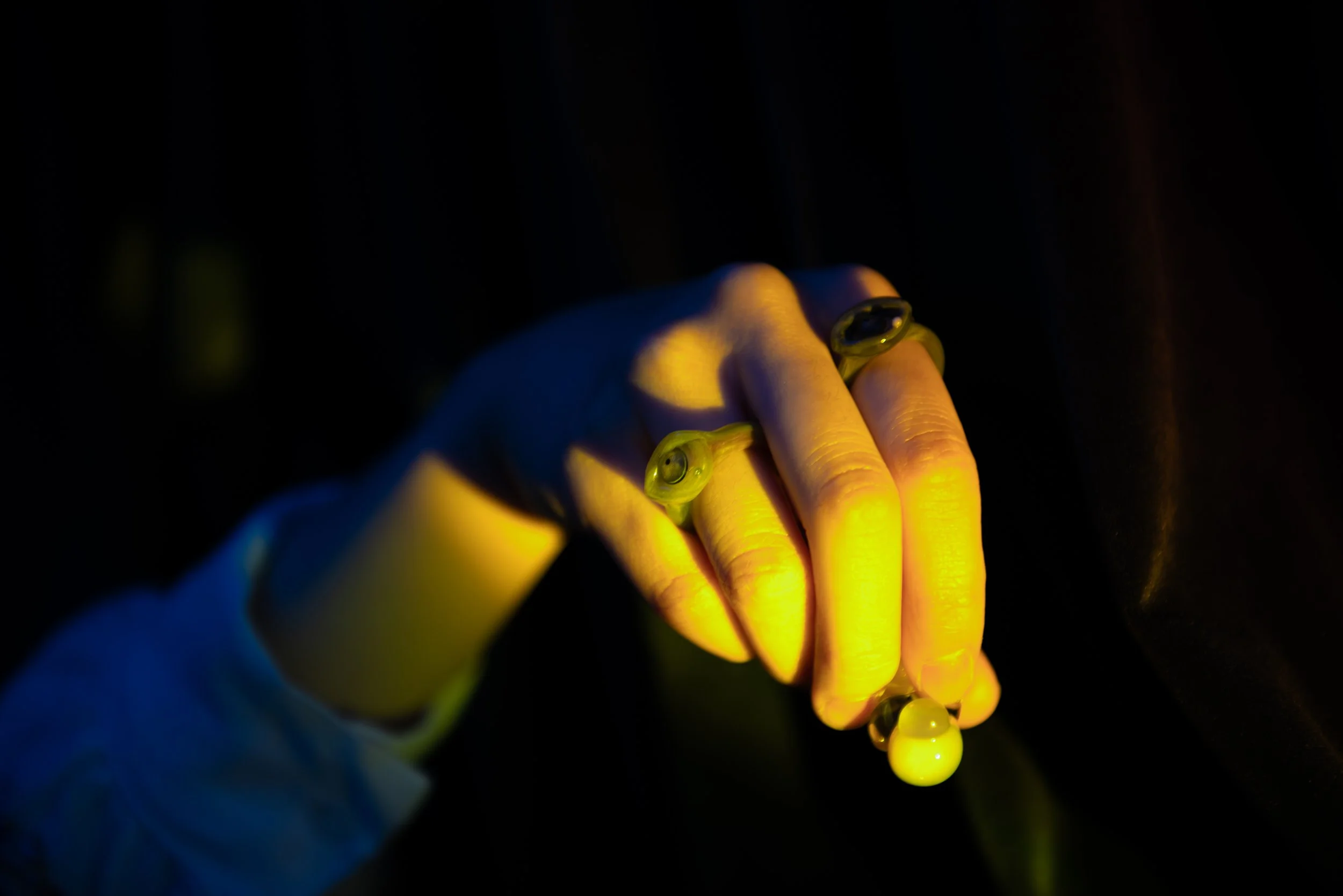 Hand wearing rings with glowing jellyfish in a dark environment.