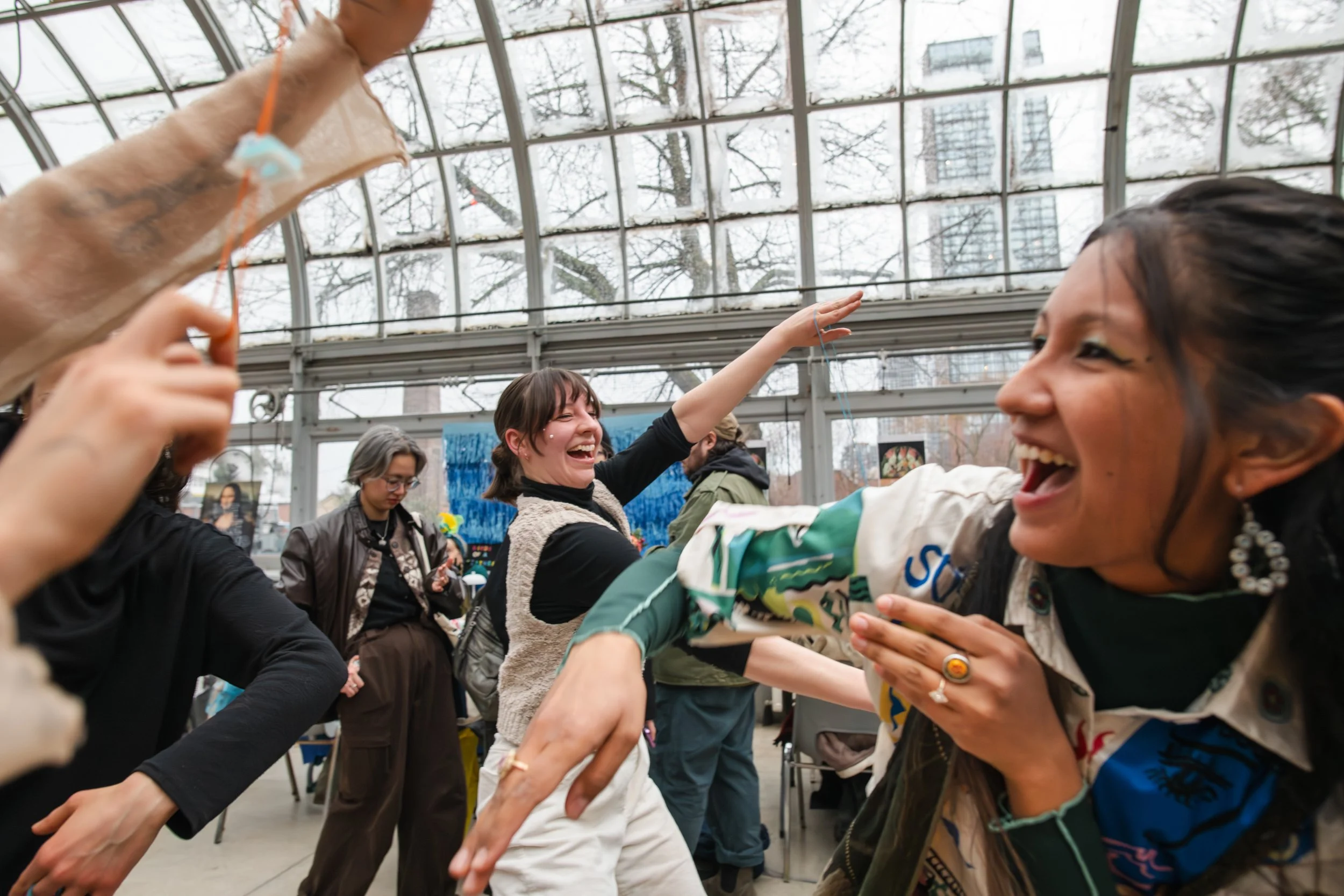 People laughing and dancing together inside a glass greenhouse or atrium.