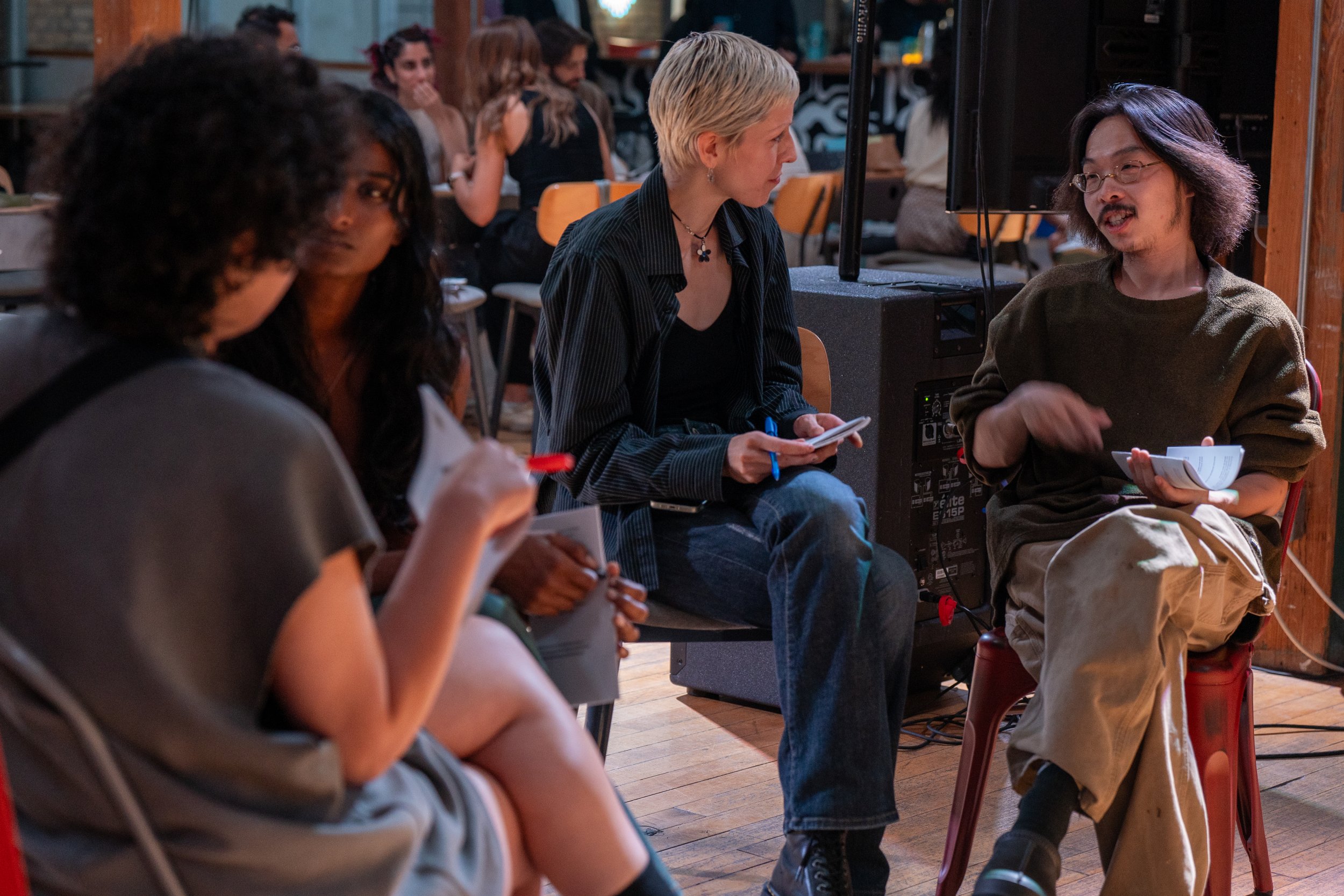 A group of people sitting in a circle engaged in discussion at an indoor event.