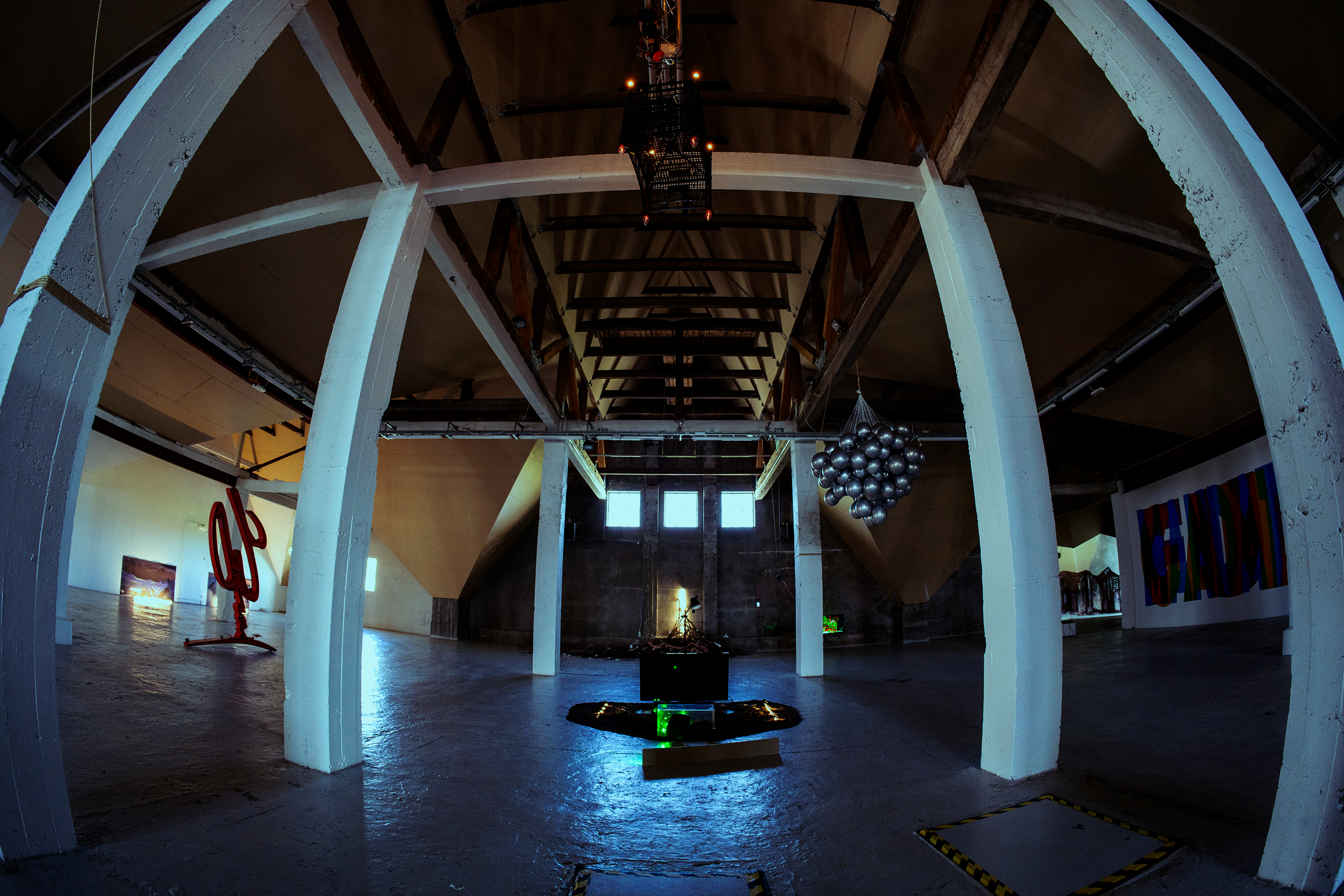 Interior of an art exhibition space with abstract sculptures, balloon installation, and modern artwork on the walls, illuminated with mixed lighting.