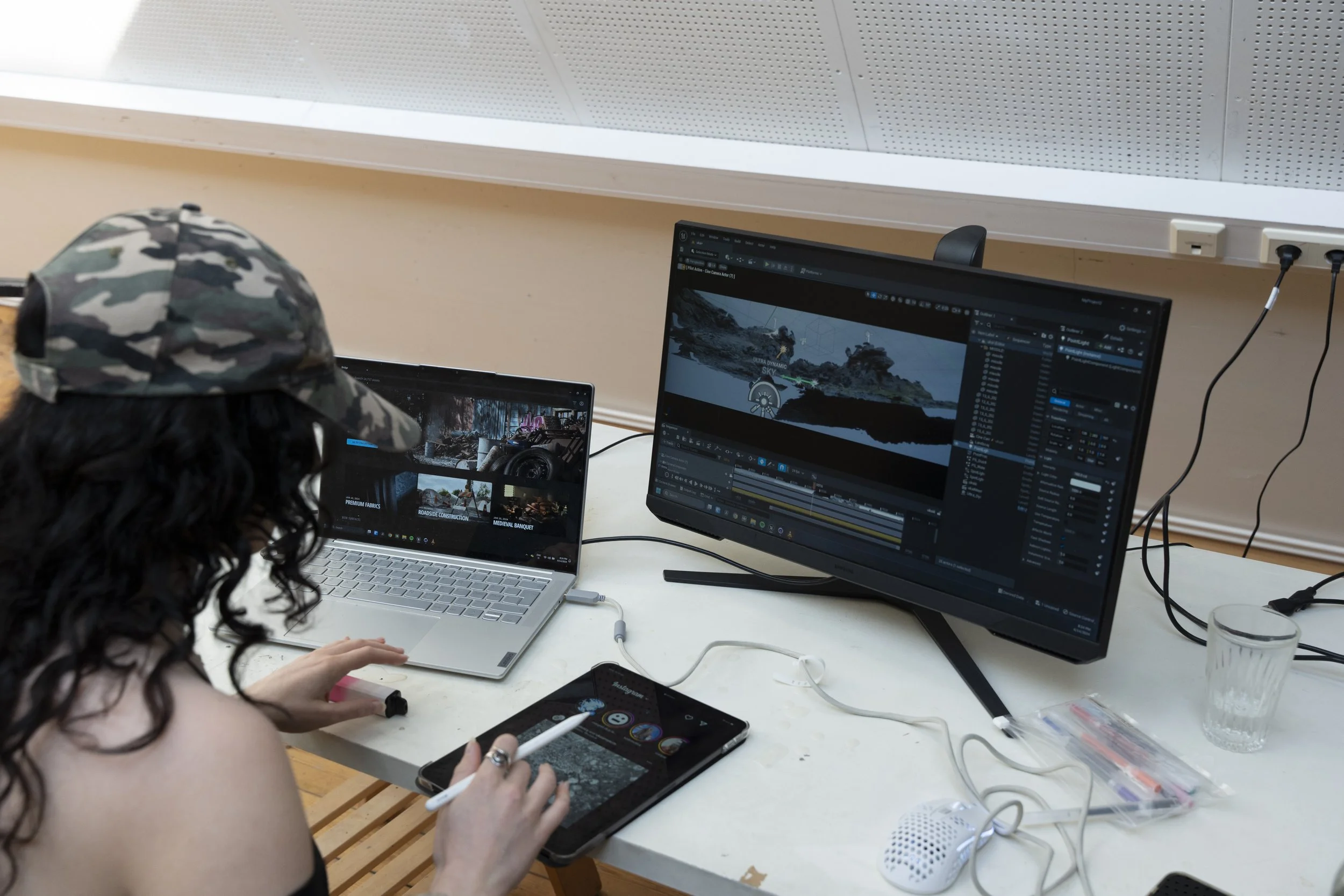A person working on video editing with multiple screens, a tablet, and a laptop on a desk in an office or studio setting.