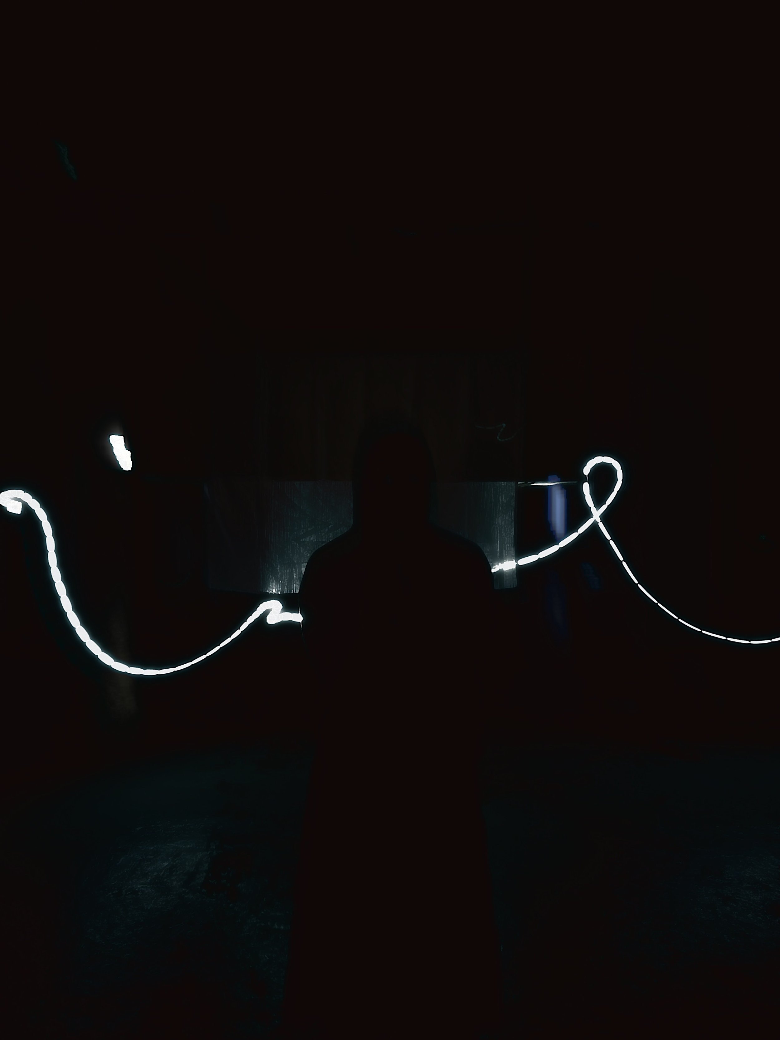 A person silhouette holding glowing, wavy light streaks in dark surroundings, creating a figure-eight or infinity shape.