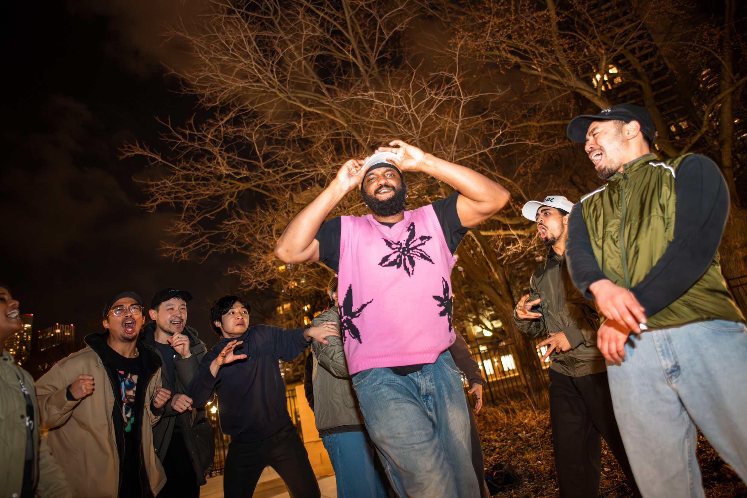 Group of people laughing and dancing outdoors at night under a large bare tree.