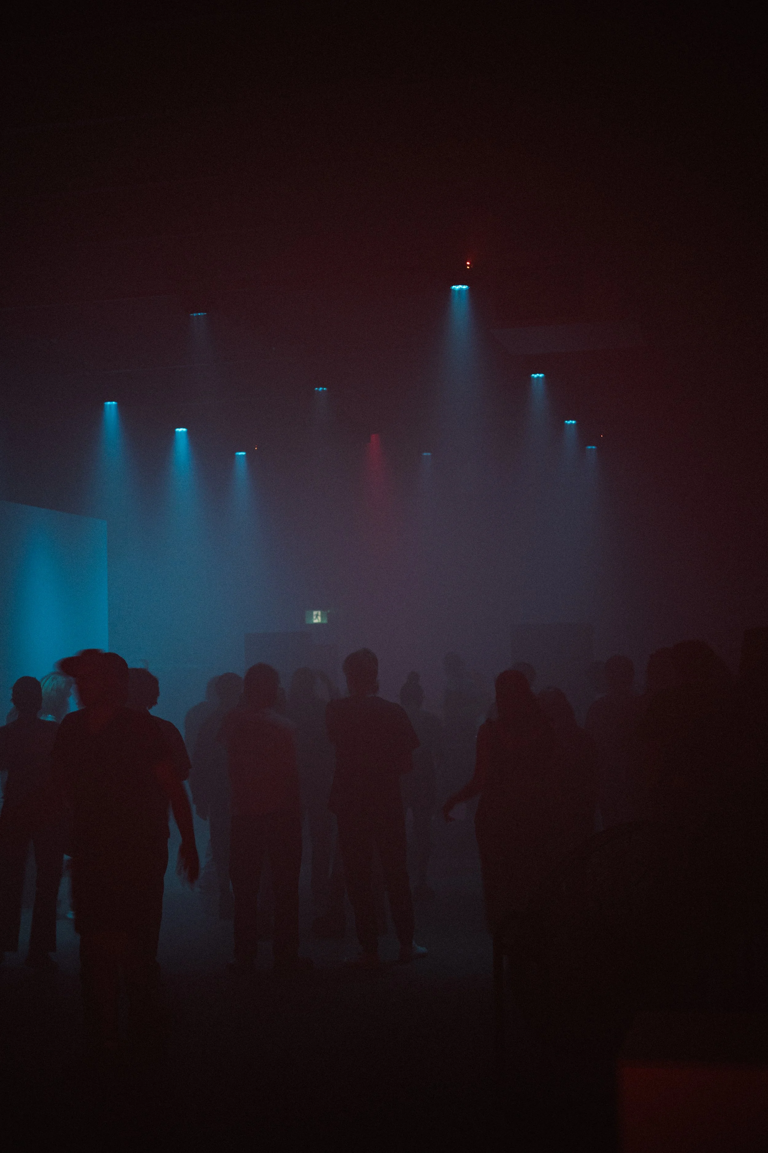 People dancing and socializing in a dark, smoky nightclub with blue and red stage lights overhead.