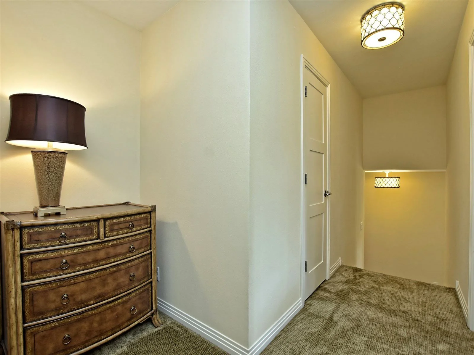 Interior hallway with a wooden dresser, table lamp, and carpeted floor