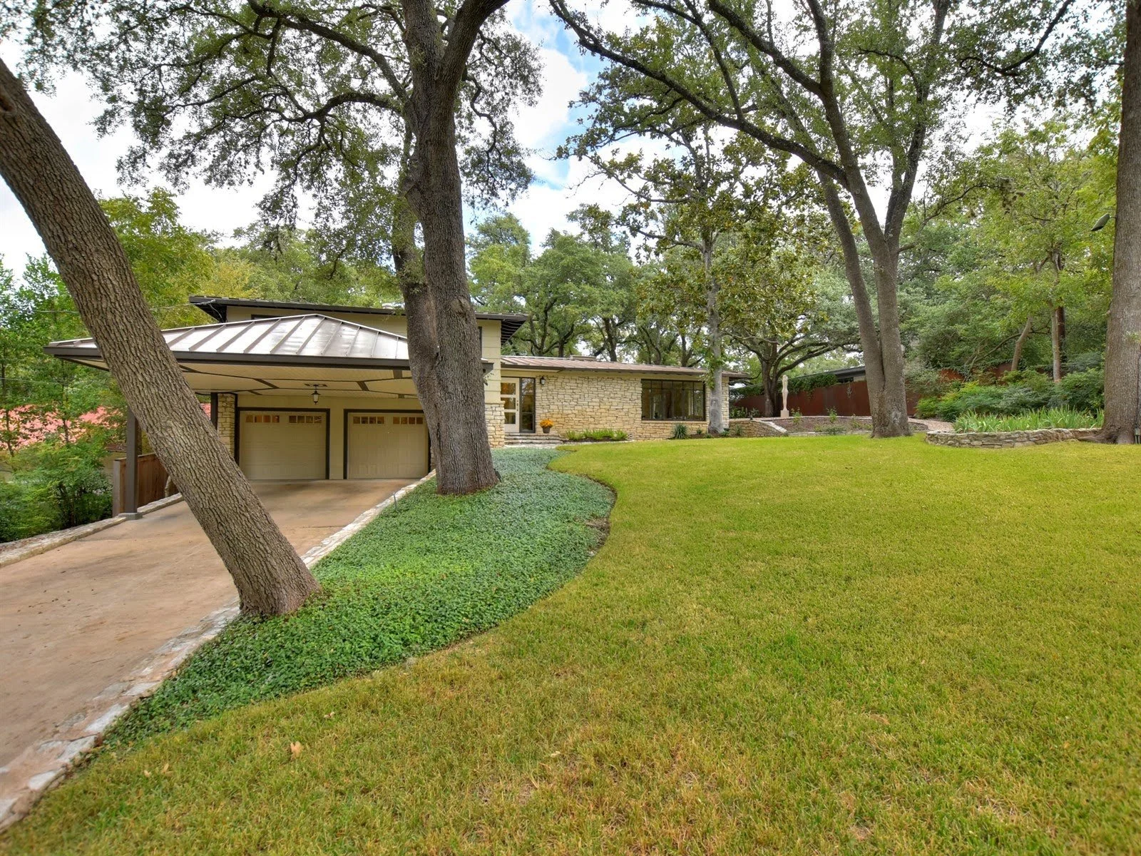 Modern house with large garage, surrounded by trees and spacious grassy yard.