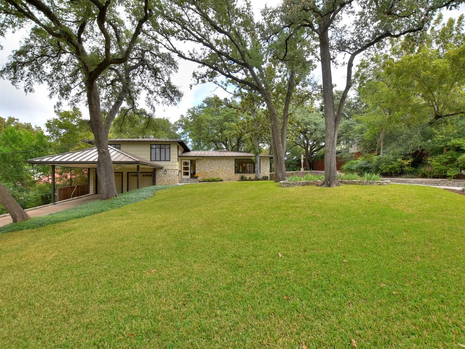 House with stone and wood exterior, surrounded by trees and large green lawn.