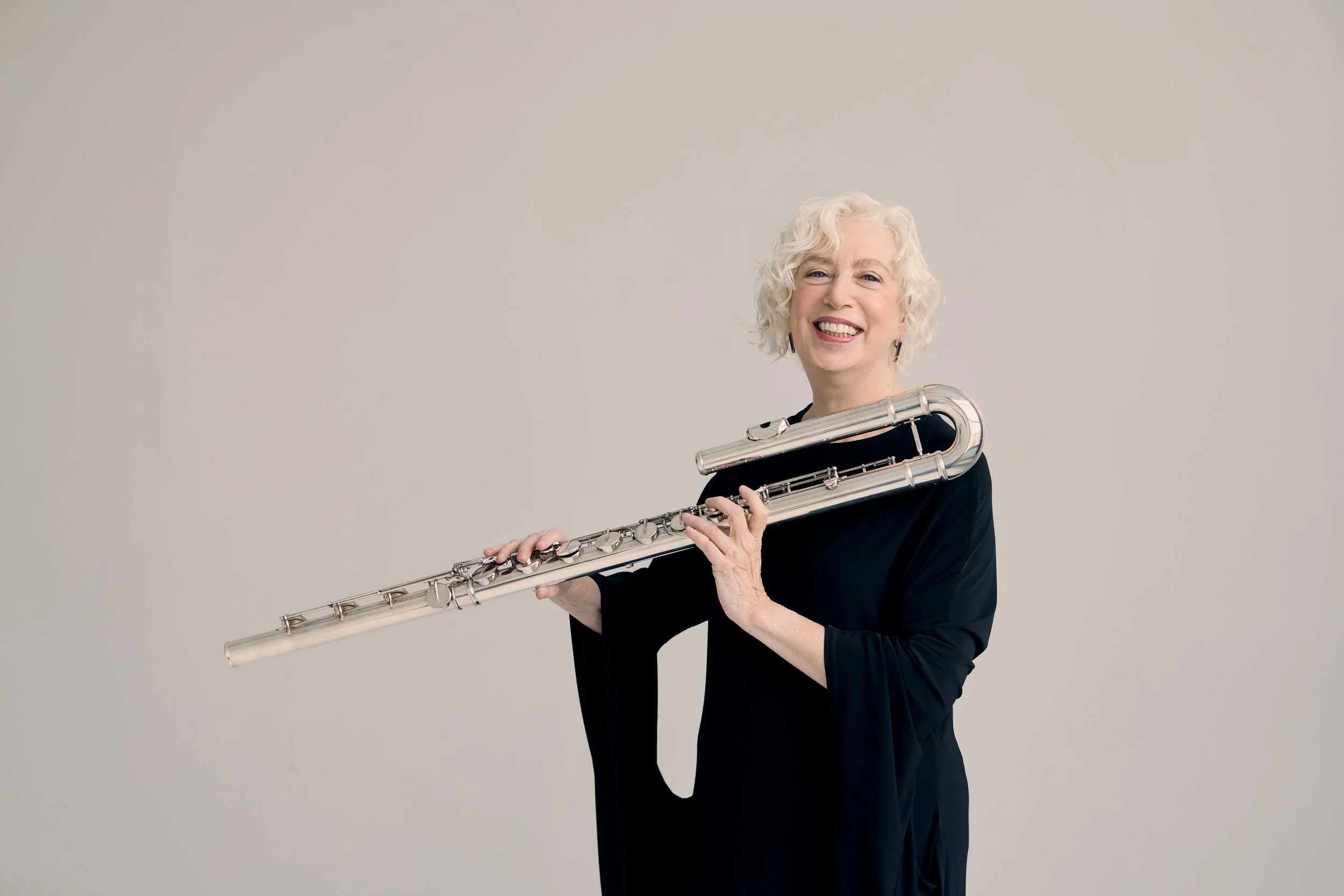 Wendy Stern, performer and educator, wearing a black dress and smiling, holding a bass flute