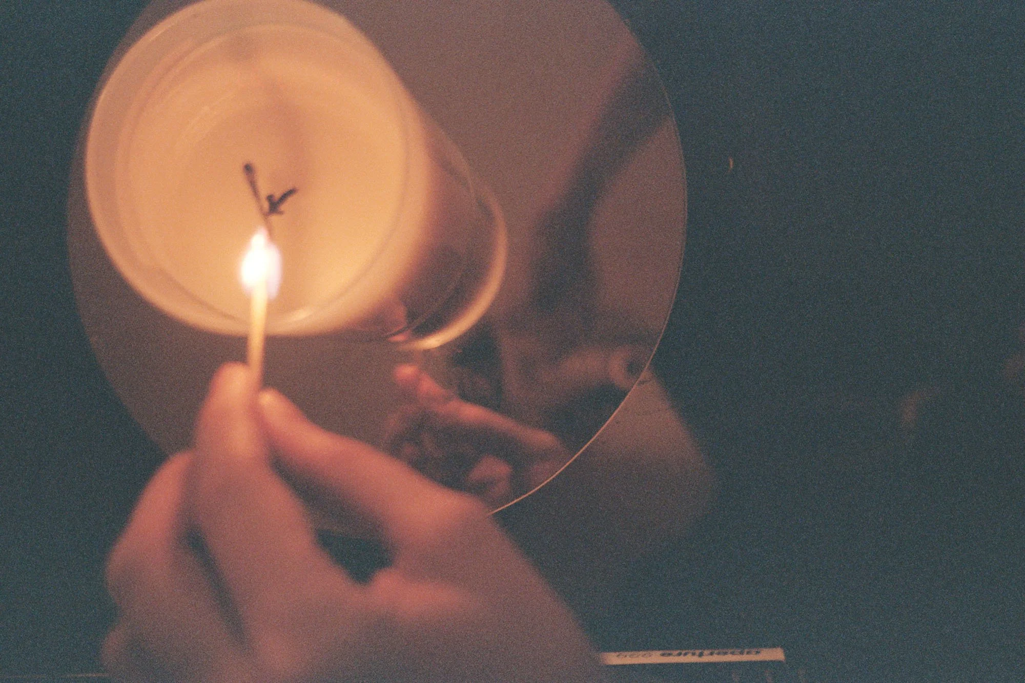 Person lighting a candle with a match, reflected in a round mirror.