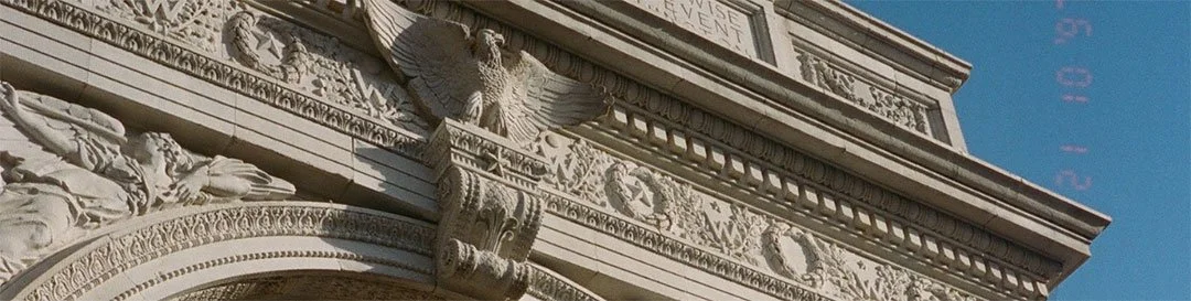 Close-up of an ornate stone building with detailed carvings, including an eagle sculpture and decorative wreaths, against a clear blue sky.