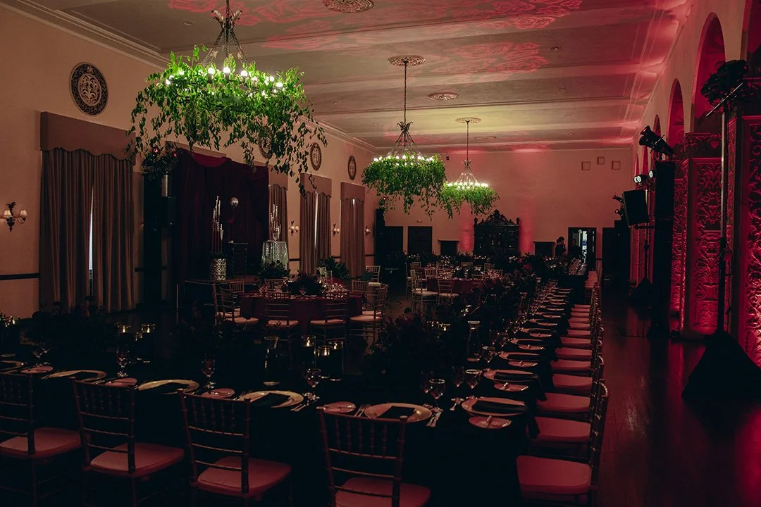 Elegant banquet hall decorated with hanging greenery chandeliers, draped curtains, and soft pink lighting, set up for a formal event.