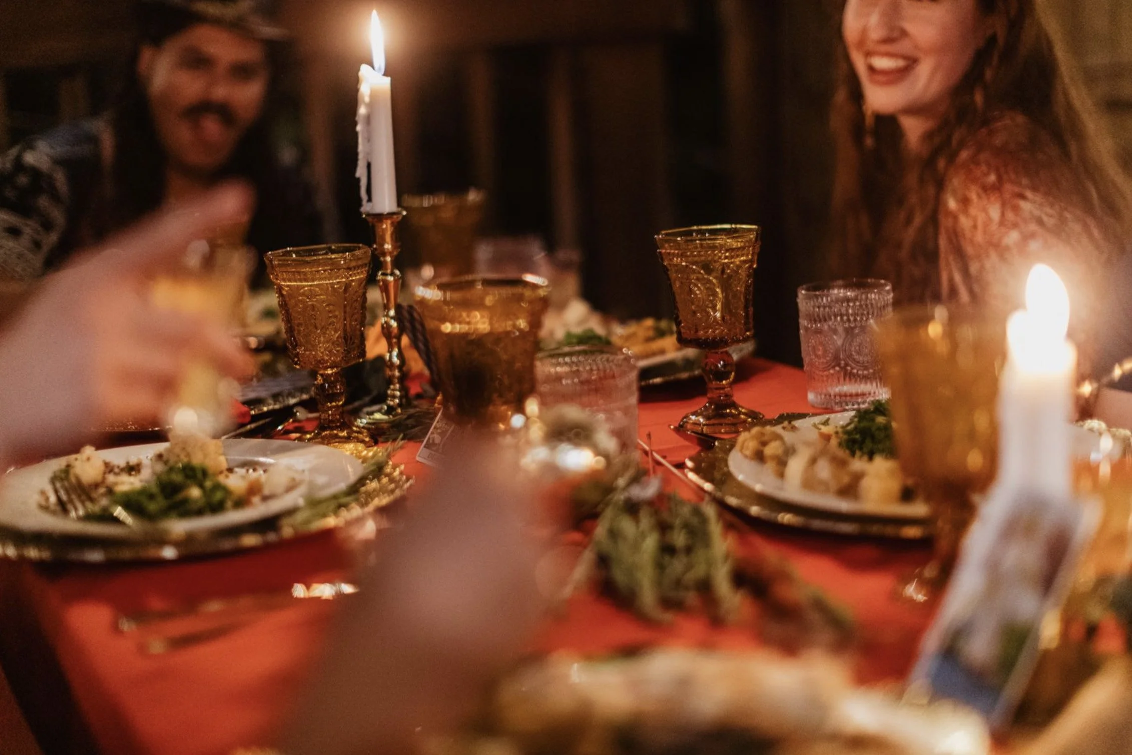 People sitting around a table enjoying a meal during a festive dinner, with lit candles and ornate glassware.