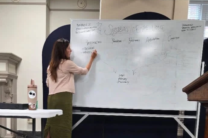 this is an image of a woman at a whiteboard giving a lecture about vocal pedagogy