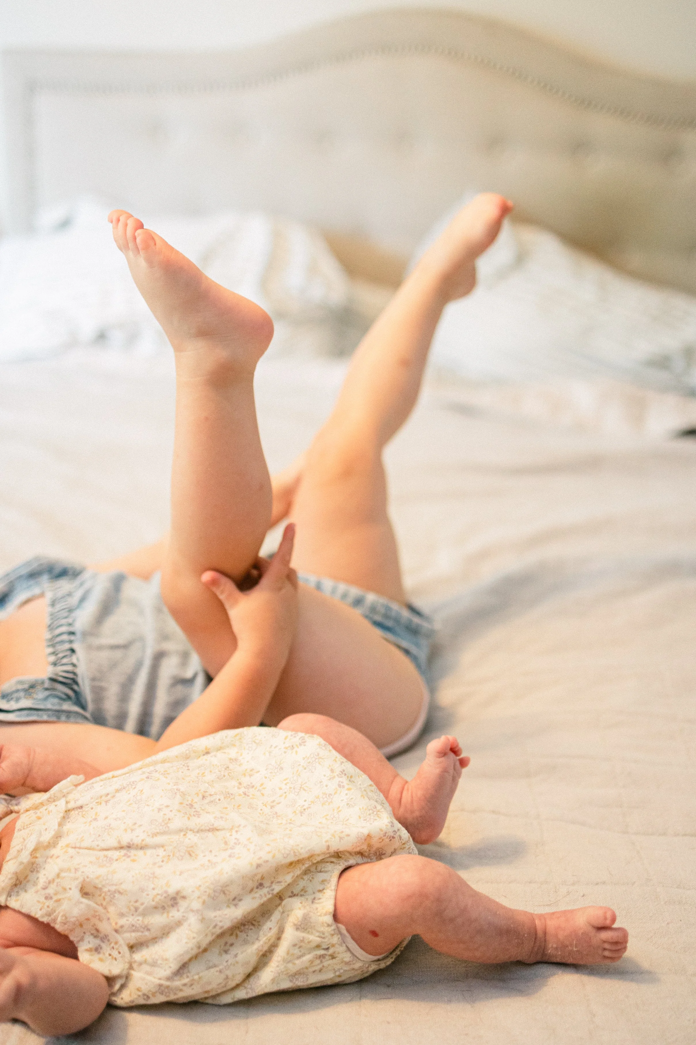 Two young children lying on a bed, playing and holding each other's legs.