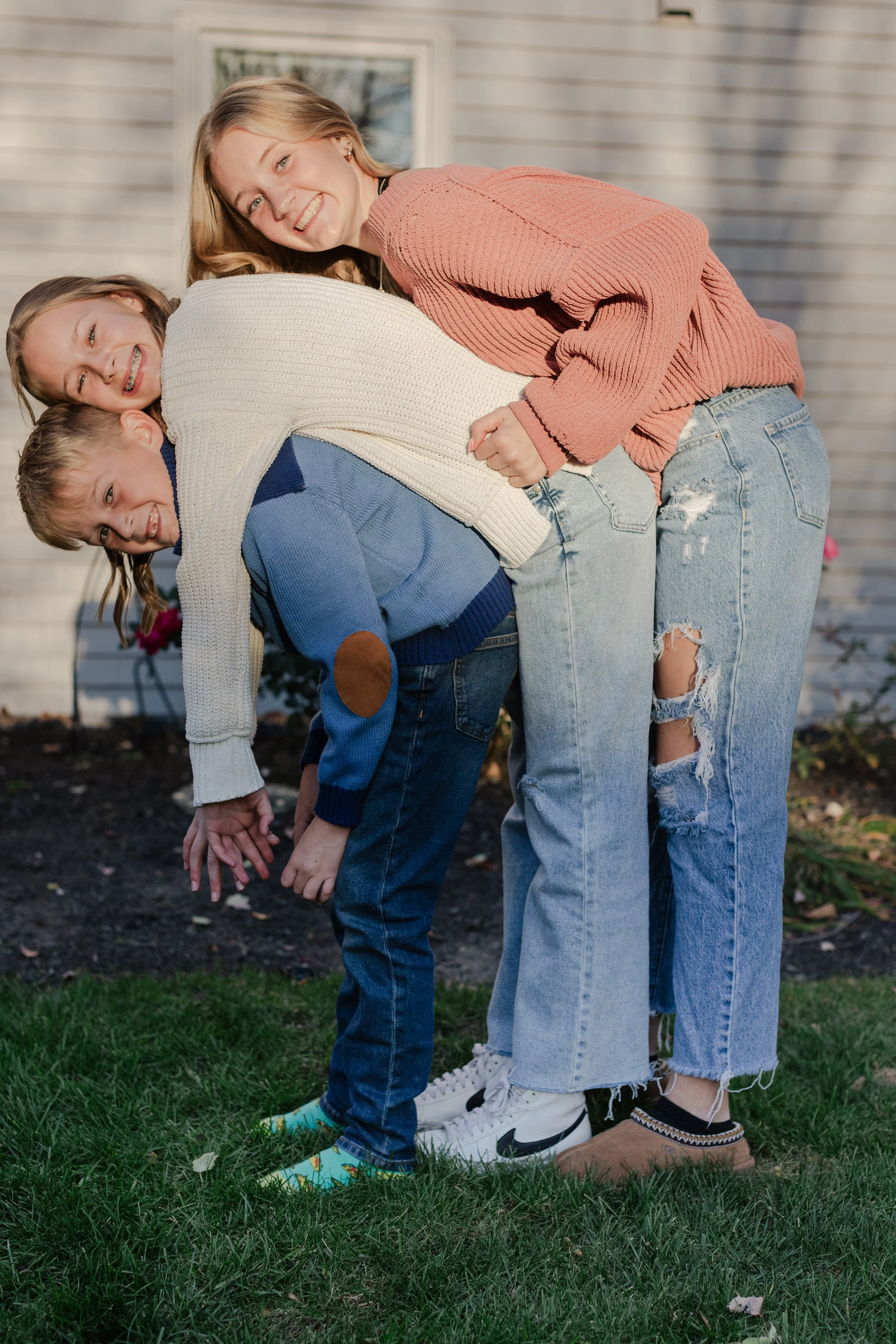Four people, two women and two children, outdoors, friends or family, playfully stacked together in a garden.