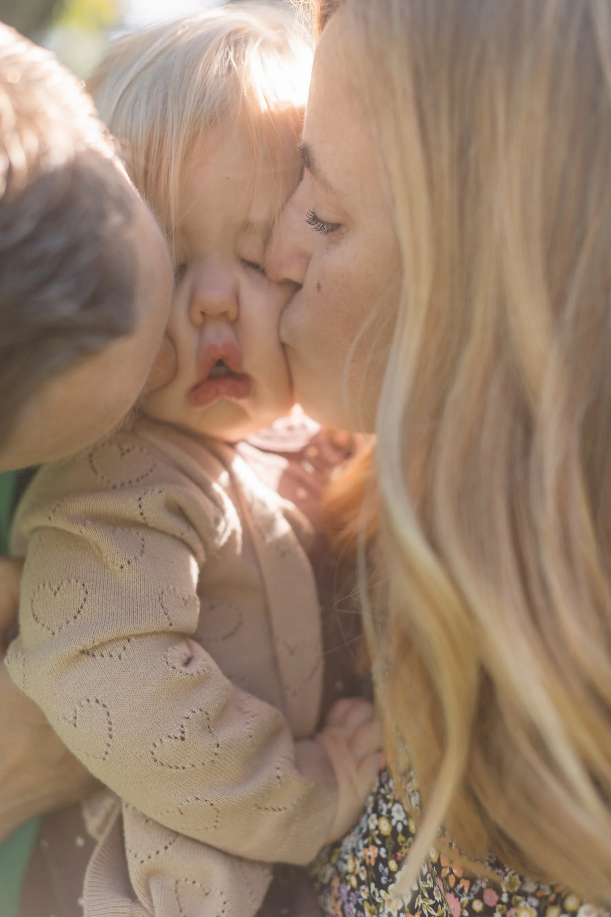 A woman kisses a young girl on the cheek, while another woman kisses the girl's cheek, showing affection.
