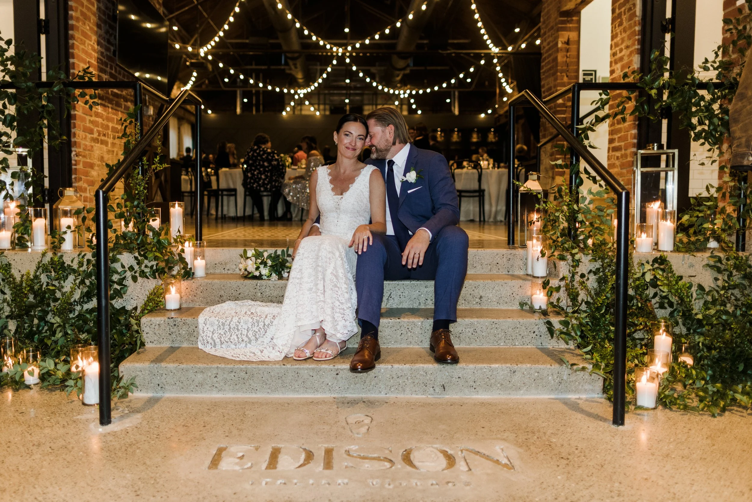 A bride and groom sitting on wedding stairs decorated with candles and greenery at Edison Hotel, celebrating their wedding reception.