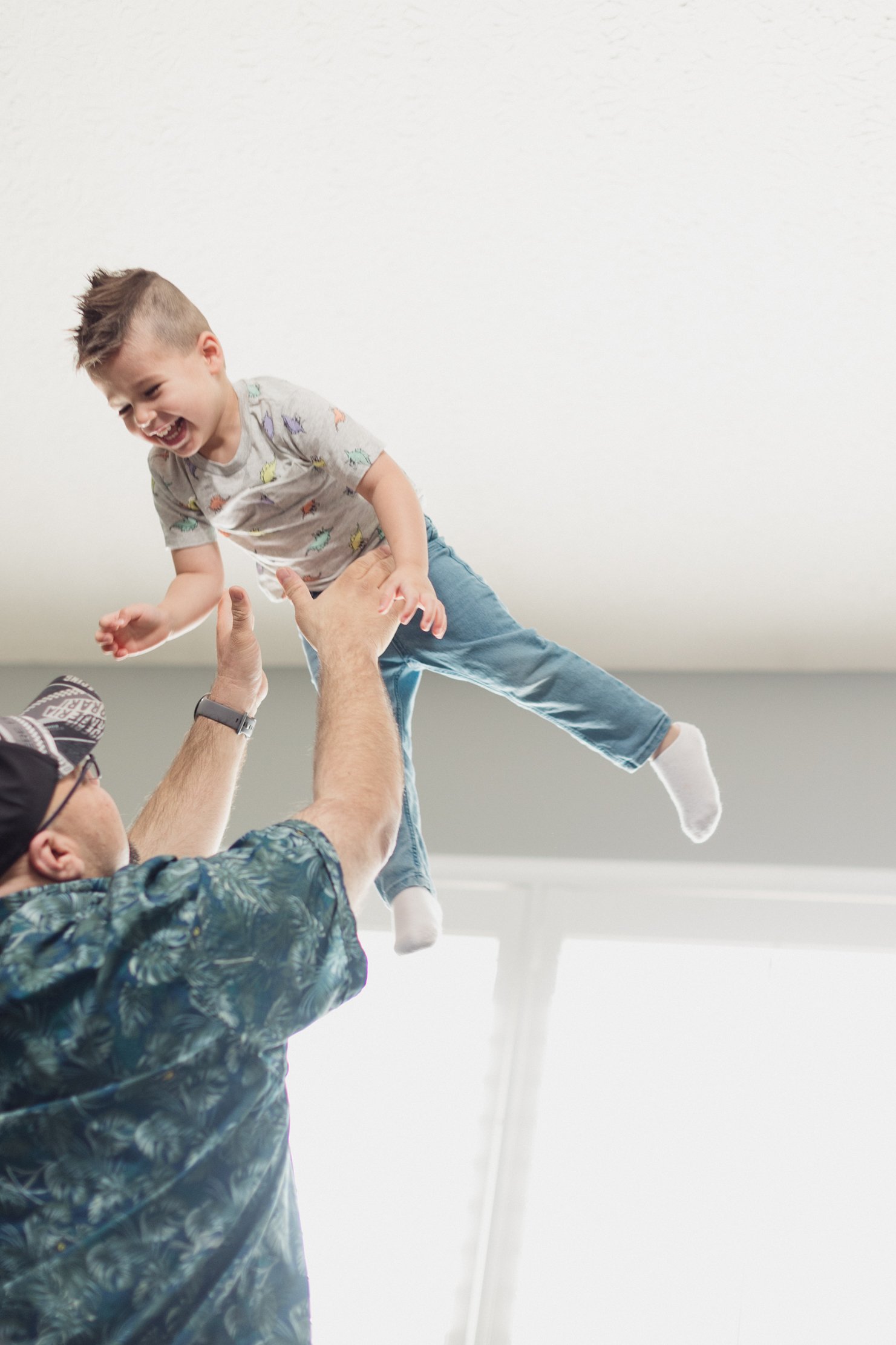 A child being thrown in the air by an adult, both smiling and enjoying their moment together indoors.
