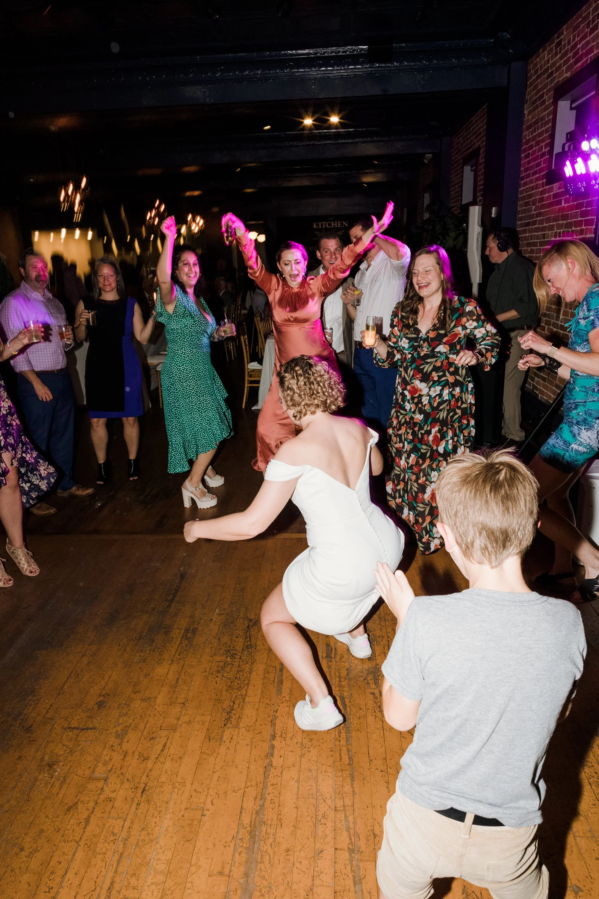 People dancing and celebrating at a party with a woman in a white dress dancing in the foreground.