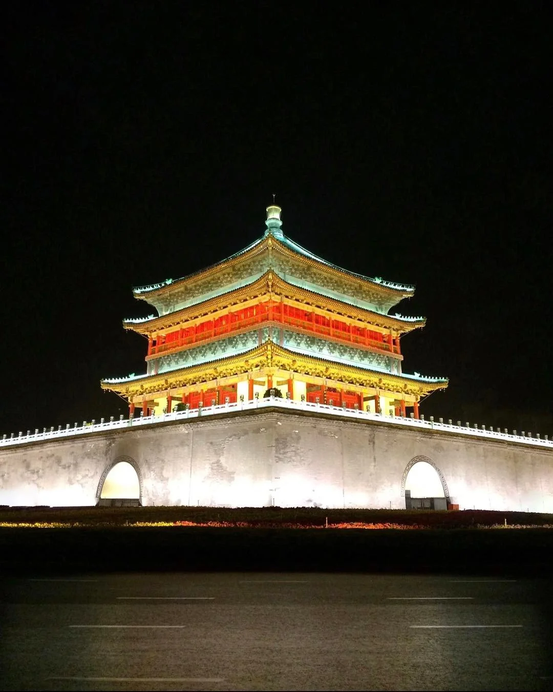 Night view of a brightly lit, traditional Chinese pagoda with multiple tiers and upturned eaves, situated on a solid stone or concrete base, against a dark sky.