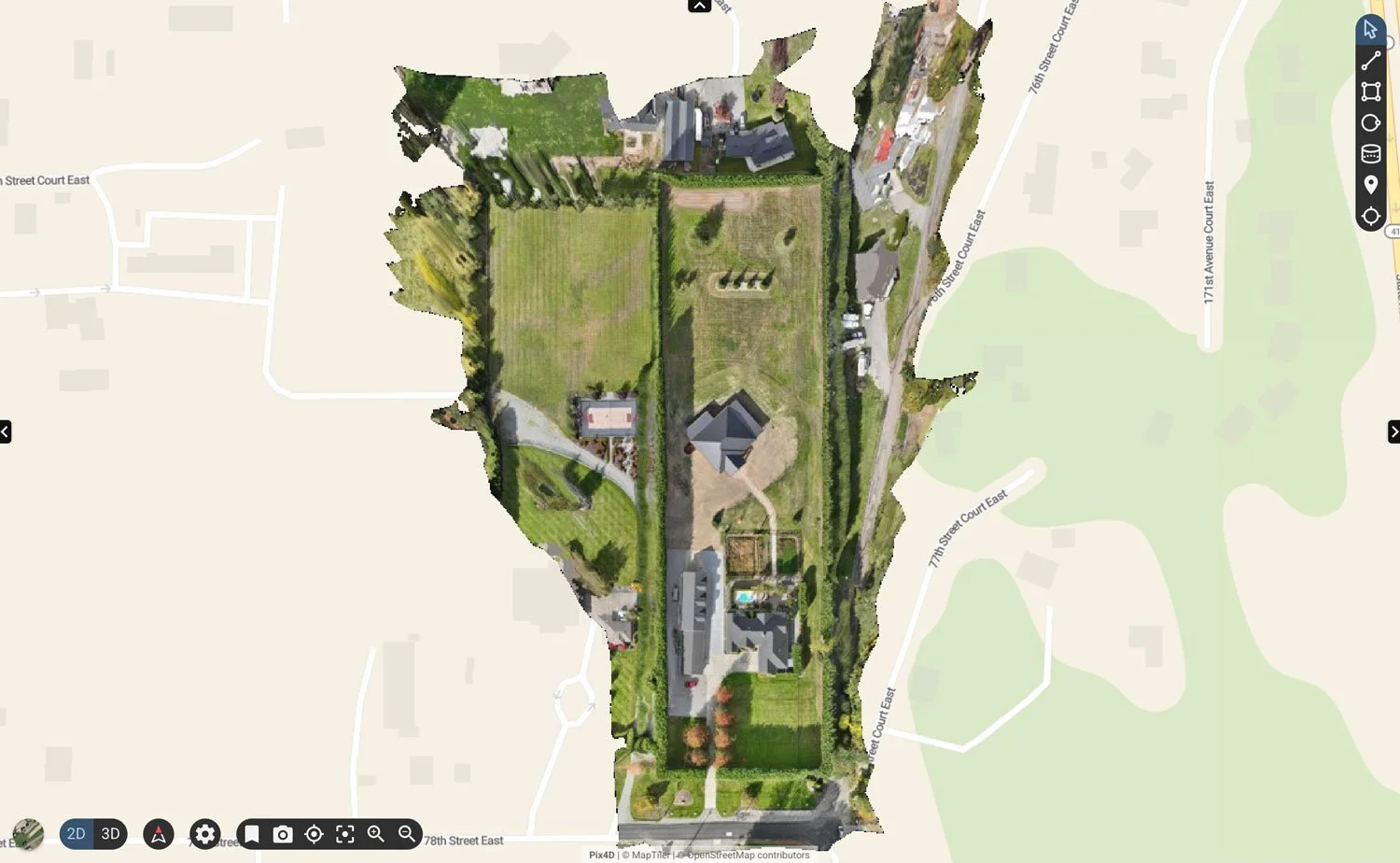 Aerial geospatial orthomosaic map of a property with multiple buildings, a large lawn, and surrounding trees, positioned on a rectangular plot with roads on three sides.