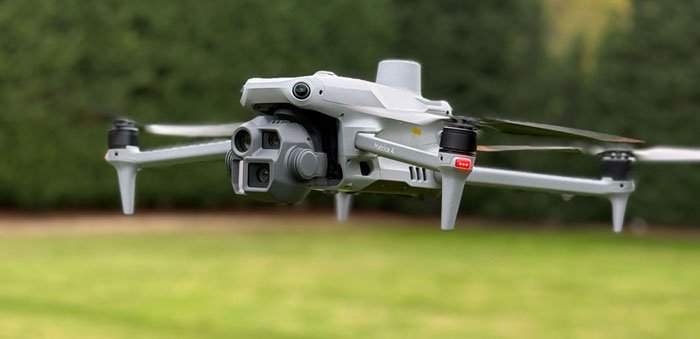 A white quadcopter drone flying outdoors over grass with a blurred green background.