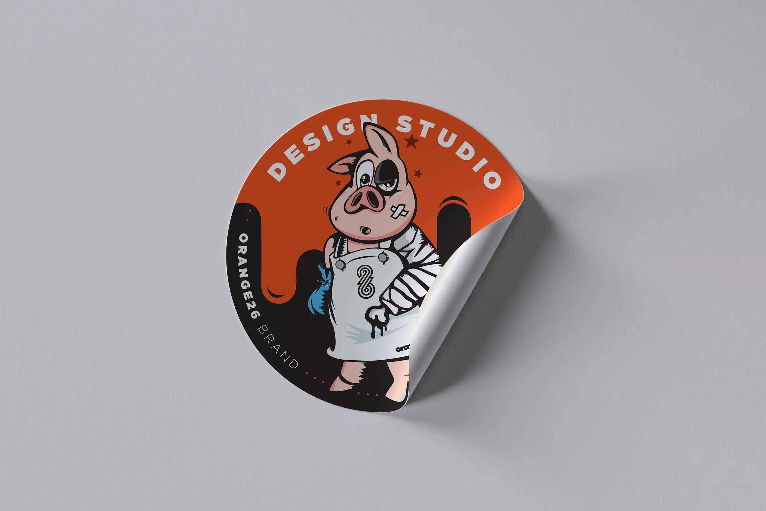 Sticker featuring a cartoon pig with a bandage on its face, wearing a zebra-patterned outfit, with text "Design Studio" on an orange background.