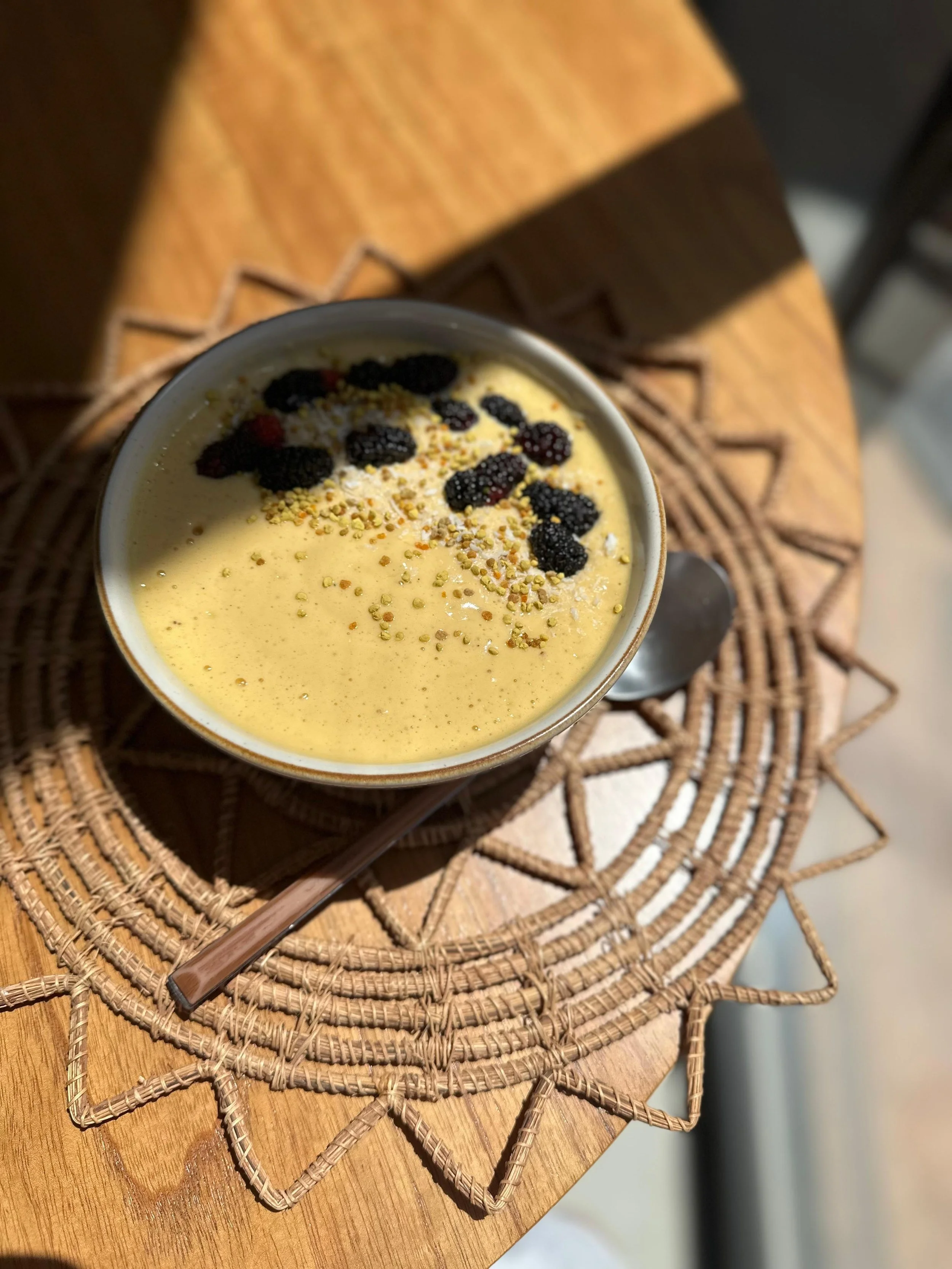 Taça com sorvete de baunilha decorada com frutas negras e confeitos coloridos, em uma mesa de madeira com toque rústico.