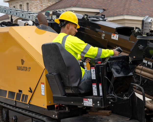 A construction worker wearing a yellow hard hat and high-visibility jacket operating heavy machinery on a construction site.