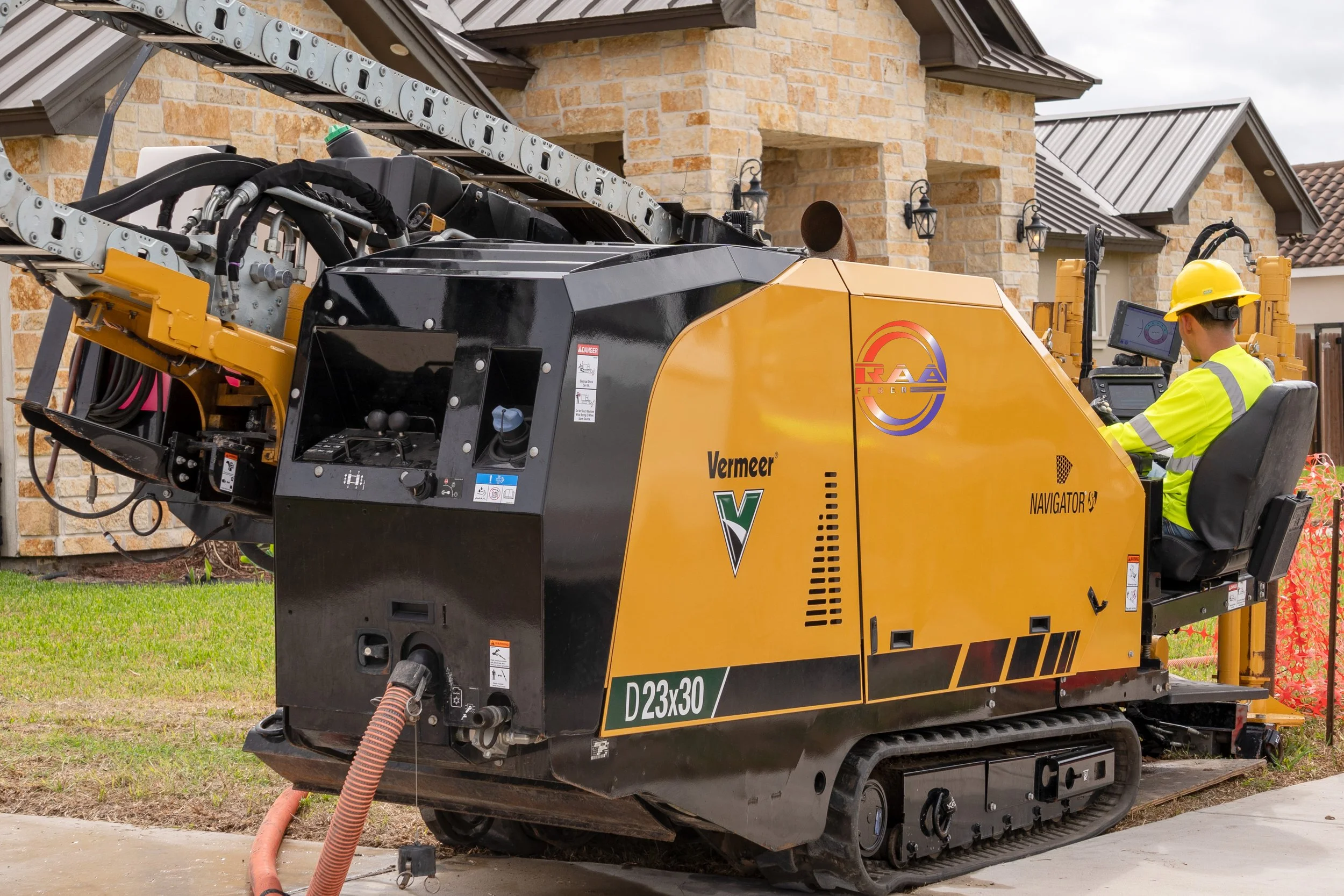 Construction worker operating a diagnosic and drilling machine with a computer screen on a residential sidewalk. The machine is yellow and black, with visible hoses and mechanical arms.