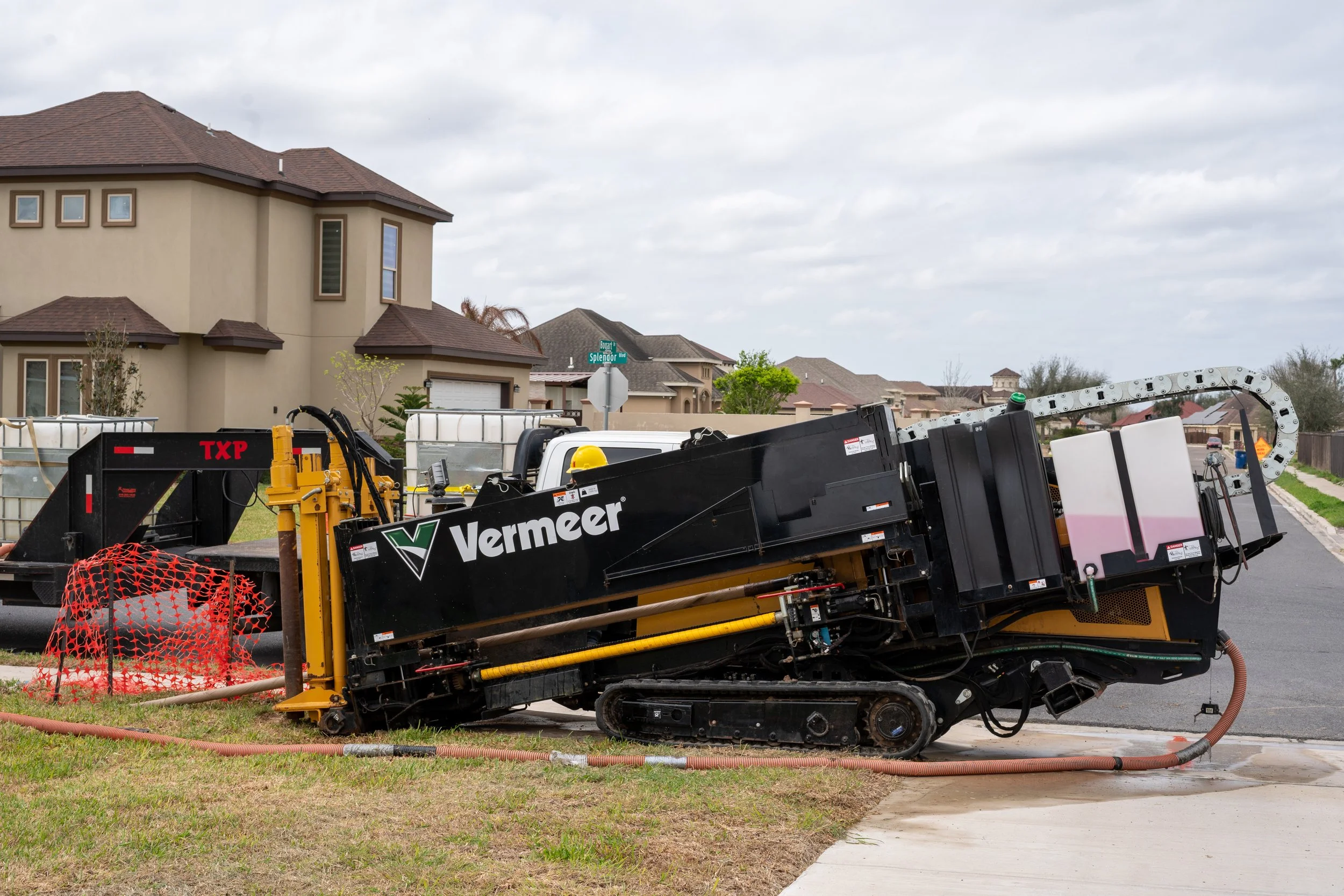 An underground utility trenching machine working on a suburban street, with houses in the background.