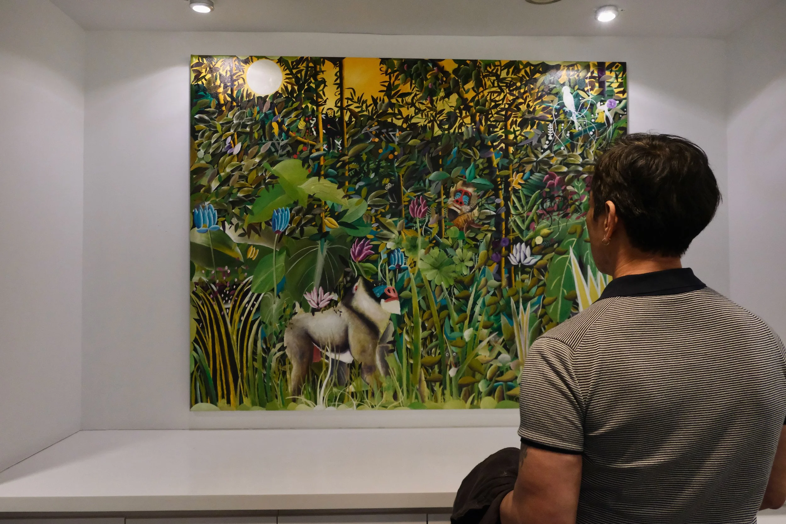 Person observing a colorful jungle scene painting with a monkey, flowers, and a bright moon.