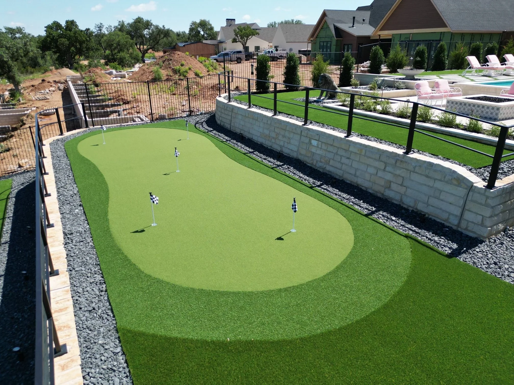 Miniature golf putting green with four checkered flags and a surrounding step and garden area in a residential backyard.