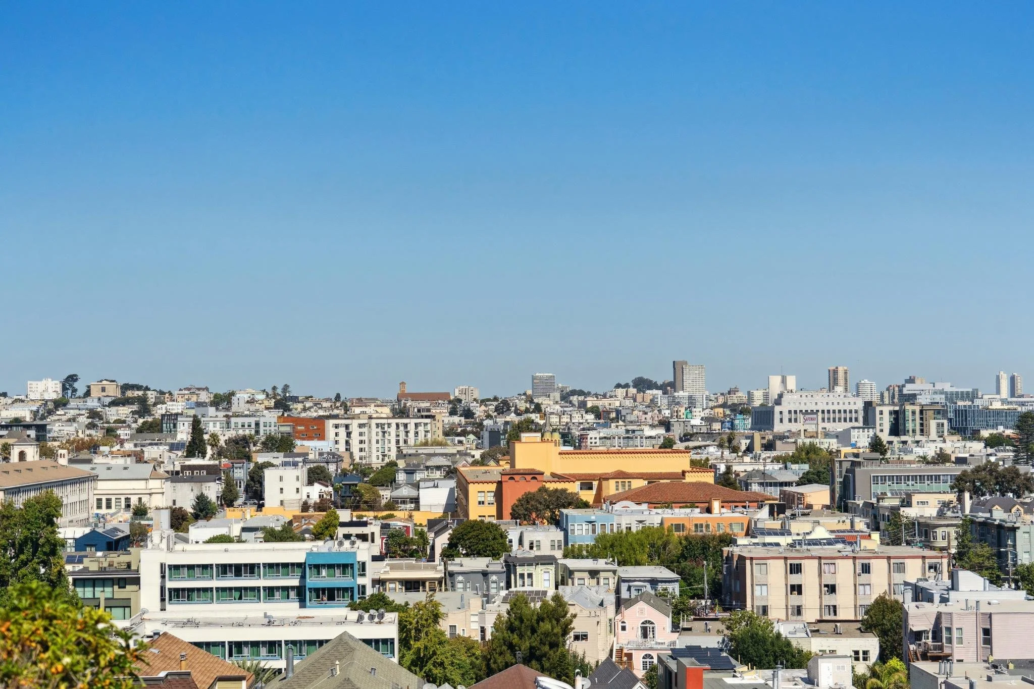 Skyline view of a city with a clear blue sky and various mid-rise buildings and houses.