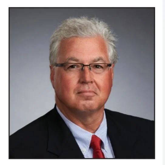 Professional headshot of David Mark Decherd wearing a dark suit, light blue shirt, and red tie.