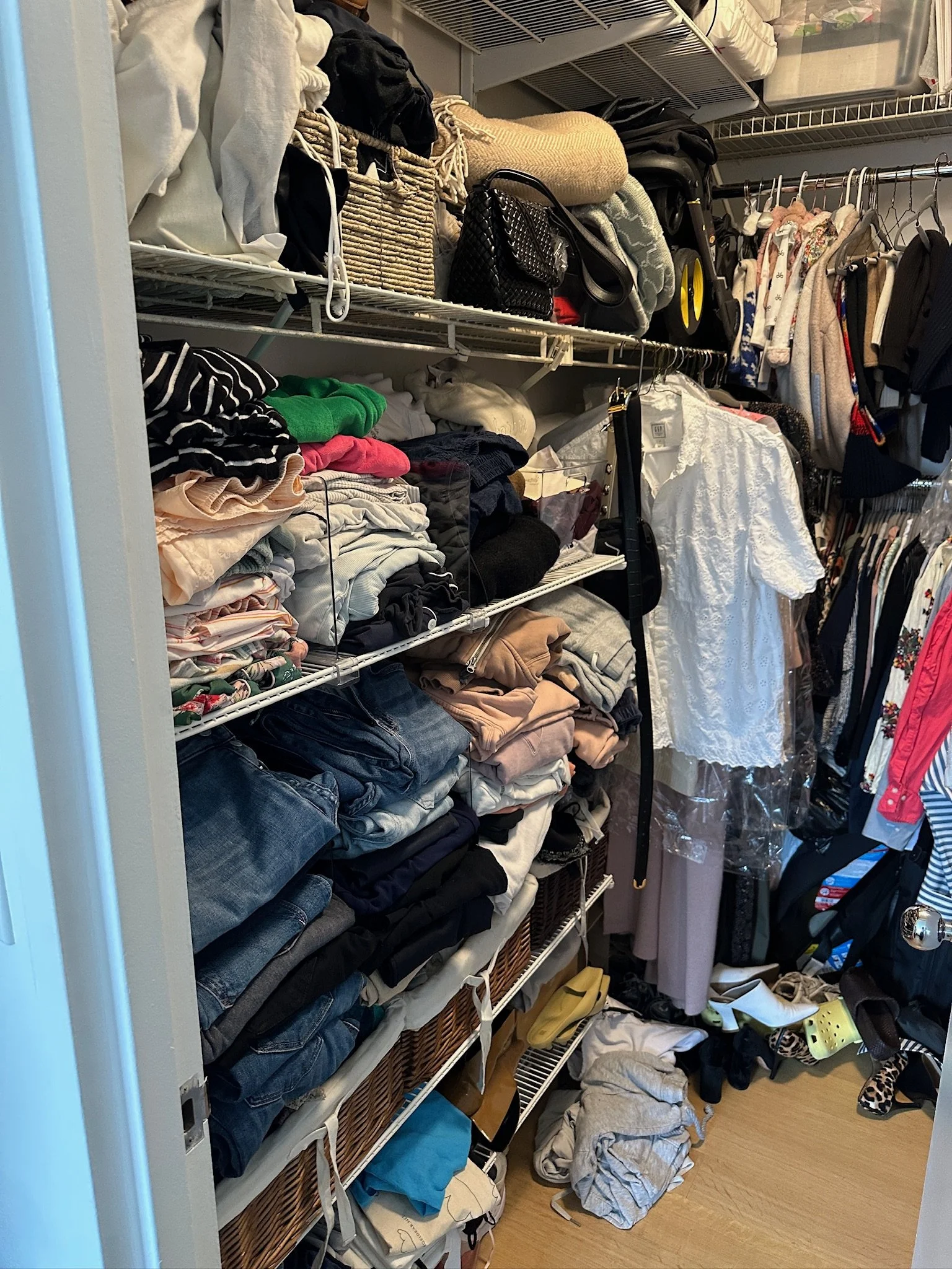 Clothes and accessories are stored on wire shelves and hanging racks in a closet, with folded shirts, pants, handbags, and shoes visible.