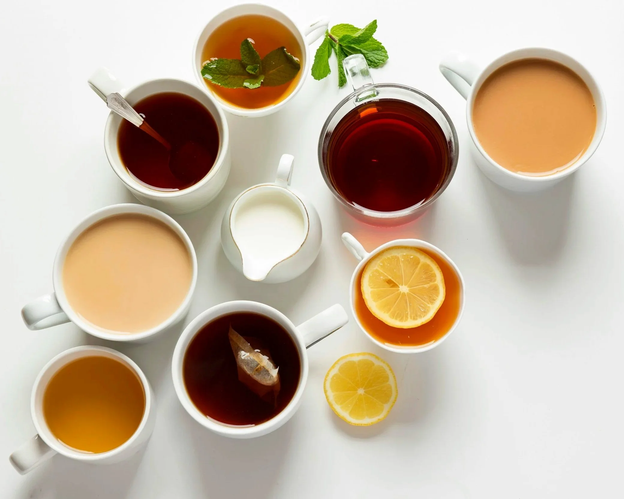 A handful of mugs shot from above filled with tea and coffee, lemon slices and mints around