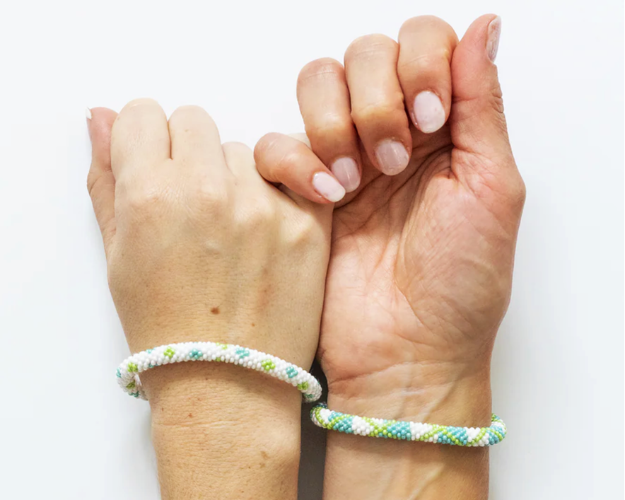 Two white hands holding pinkies and wearing matching bracelets